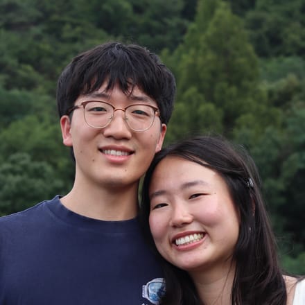 Justin smiling outdoors with a companion, in front of a wooded hillside
